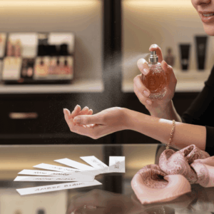 Woman testing a perfume on her wrist in a luxury boutique with blotters in the foreground.