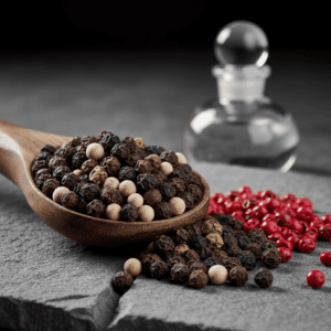 Wooden spoon filled with peppercorns of different colors (black, white, green) and pink berries, illustrating the perfumer's spicy palette.