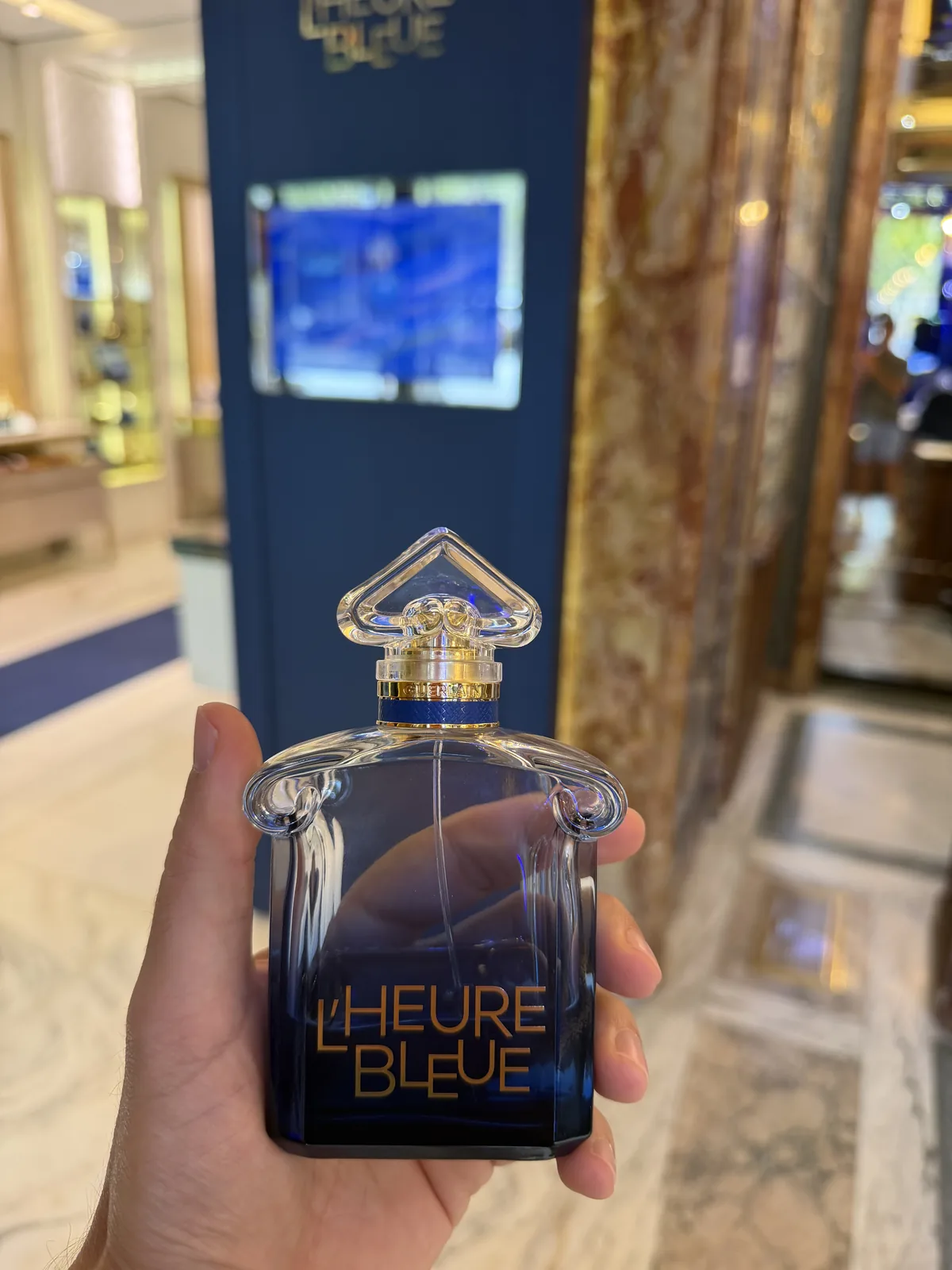 Flacon dégradé bleu de L'Heure Bleue 2026 de Guerlain tenu en main en boutique.