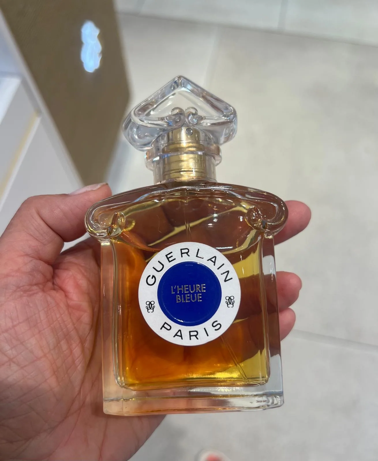 Flacon de L'Heure Bleue dans sa version classique, au jus ambré et à l'étiquette ronde bleue.