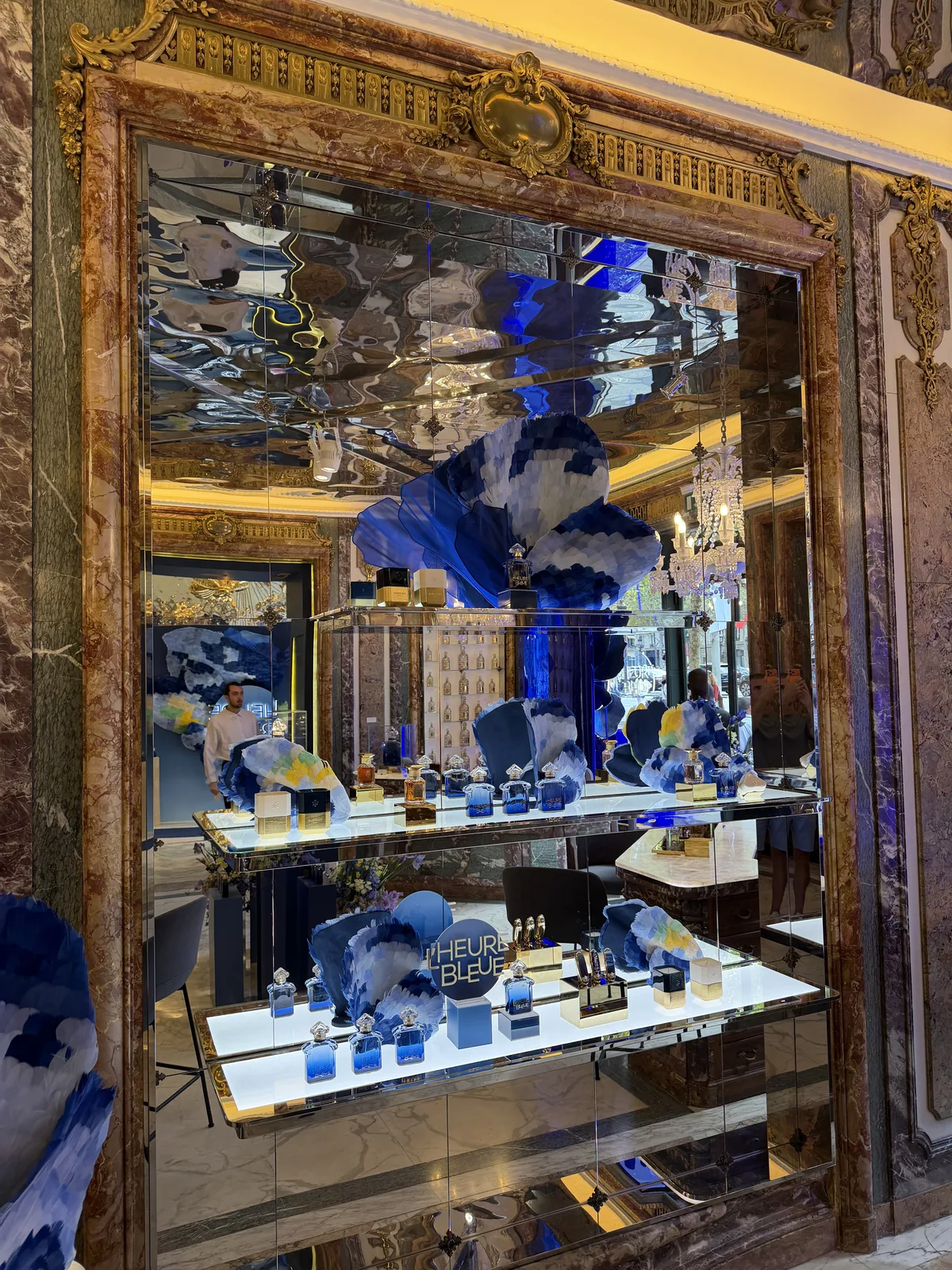 Présentoir L'Heure Bleue et pétales peints reflétés dans les miroirs de la boutique Guerlain.