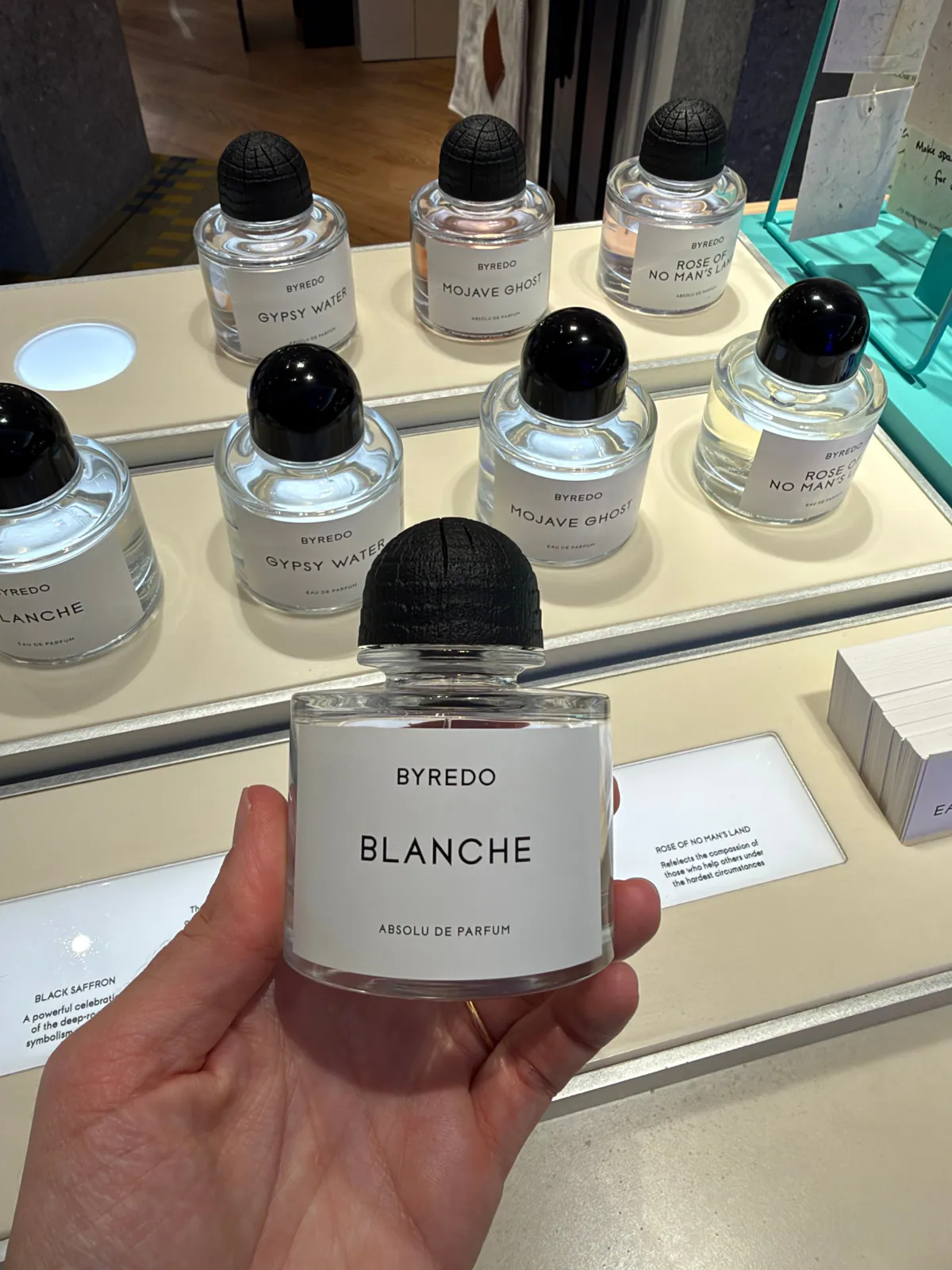 Flacon de Blanche de Byredo en absolu de parfum, tenu en main devant la table des parfums.