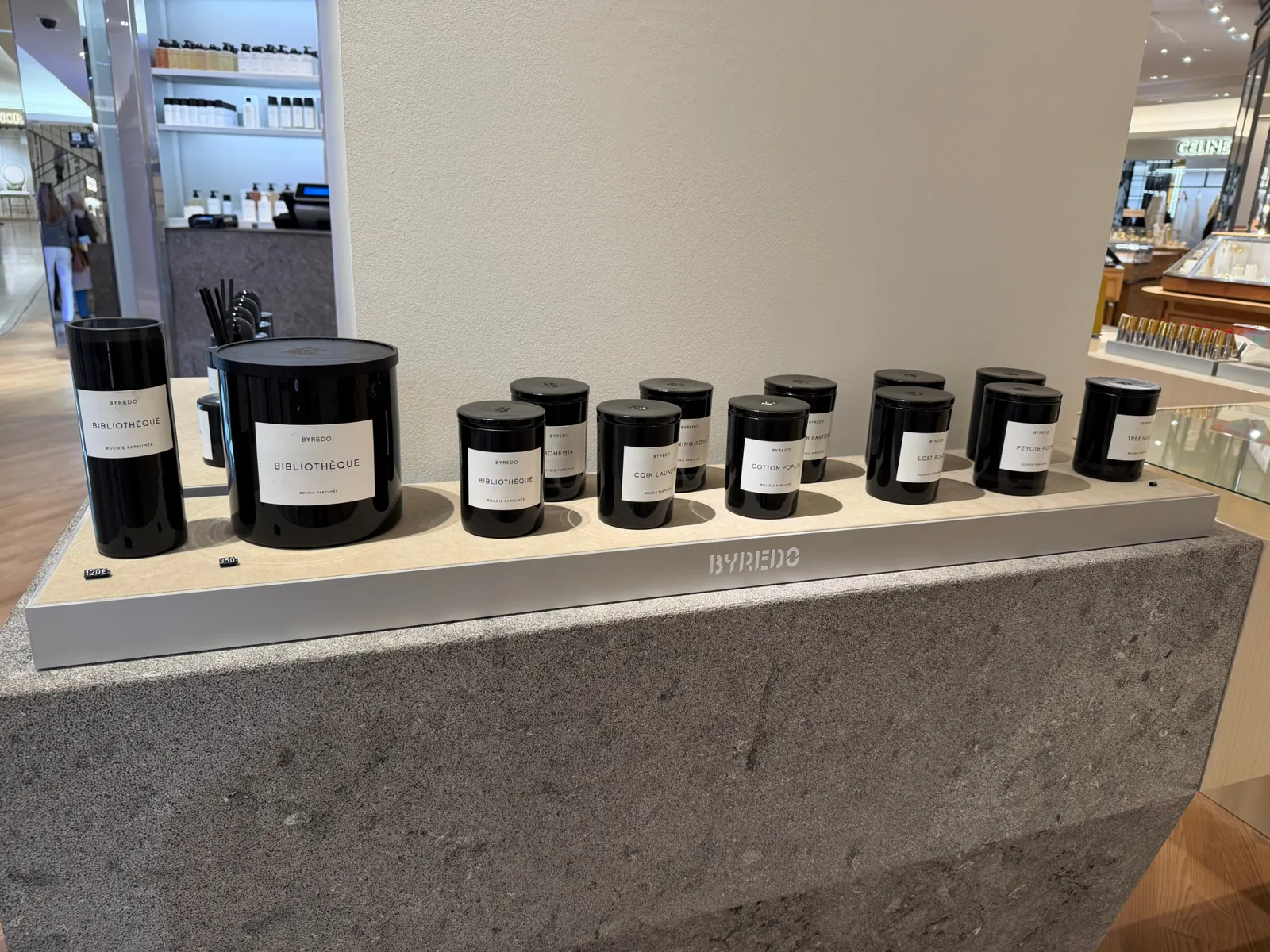 Bougies parfumées Byredo aux étiquettes blanches alignées sur un présentoir en pierre.