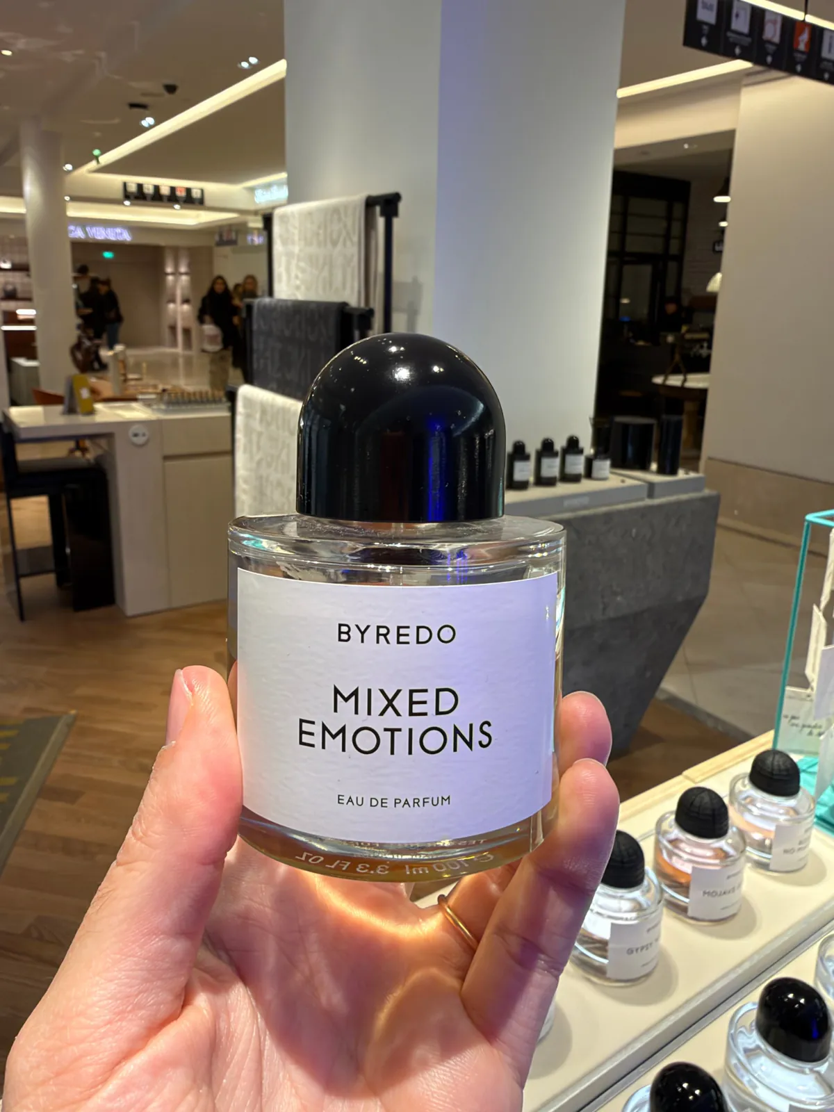 Flacon d'eau de parfum Mixed Emotions de Byredo tenu en main dans le grand magasin.