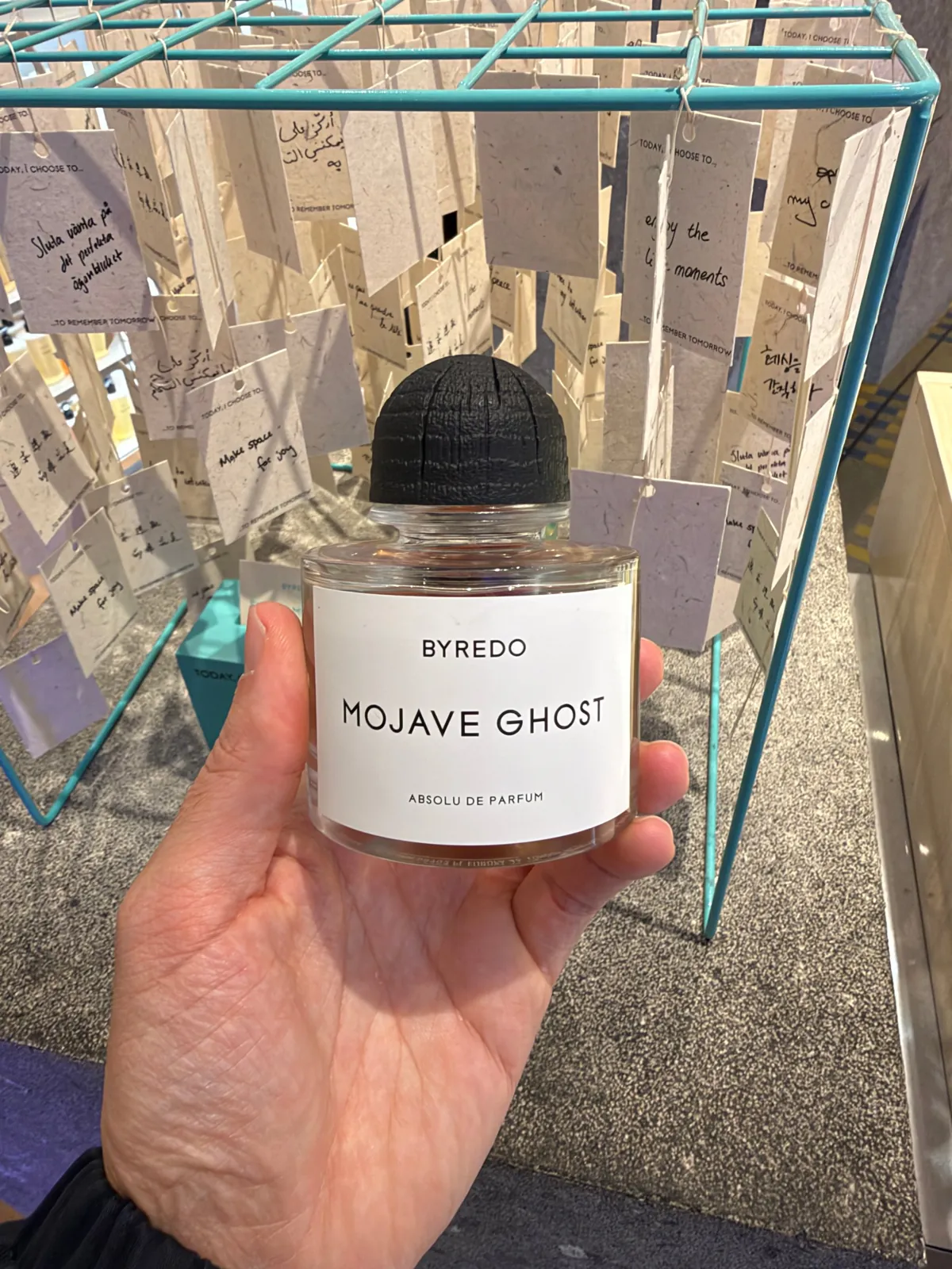 Flacon de Mojave Ghost de Byredo en absolu de parfum devant une installation de cartes suspendues.