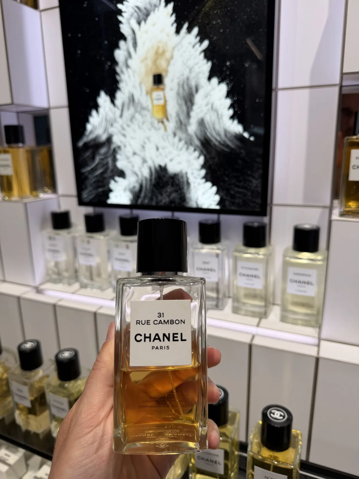 Flakon von 31 Rue Cambon von Chanel in der Hand, vor der Wand der Exclusifs.