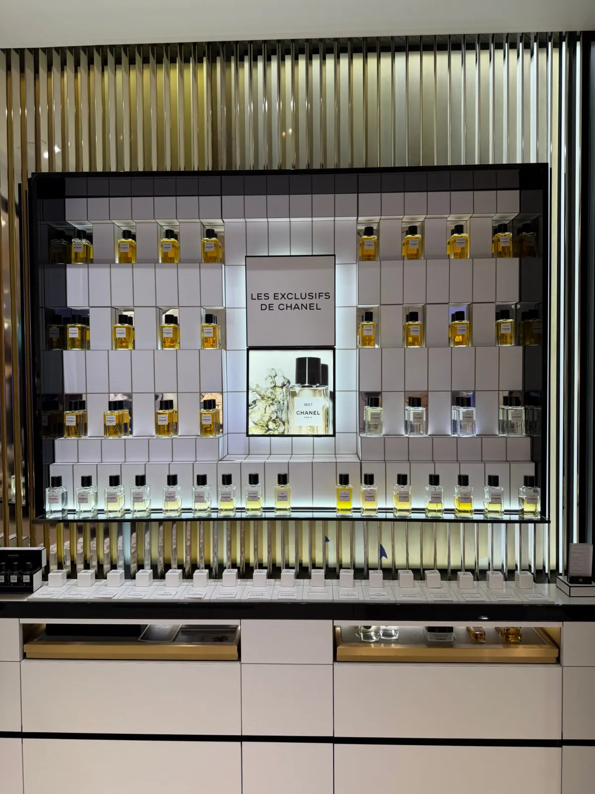 Mur des Exclusifs de Chanel avec ses flacons alignés sur des étagères blanches.