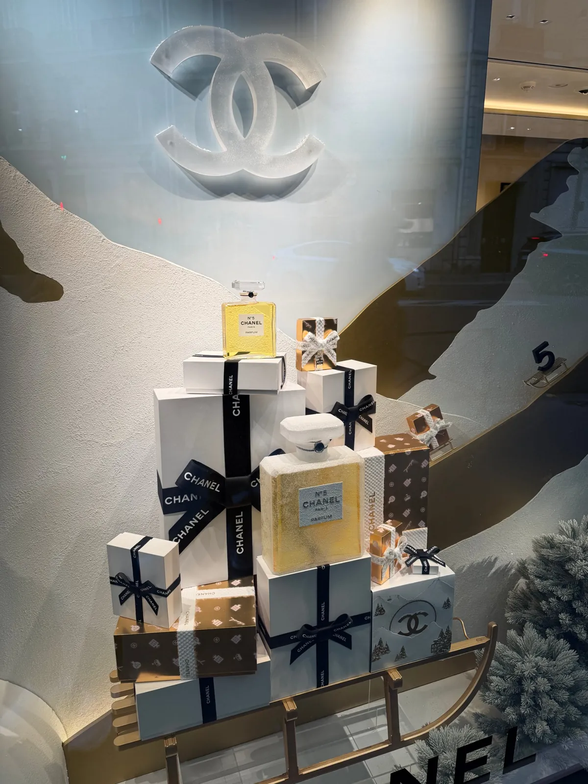 Vitrine de Noël Chanel avec des flacons de N°5 et des paquets cadeaux posés sur une luge.