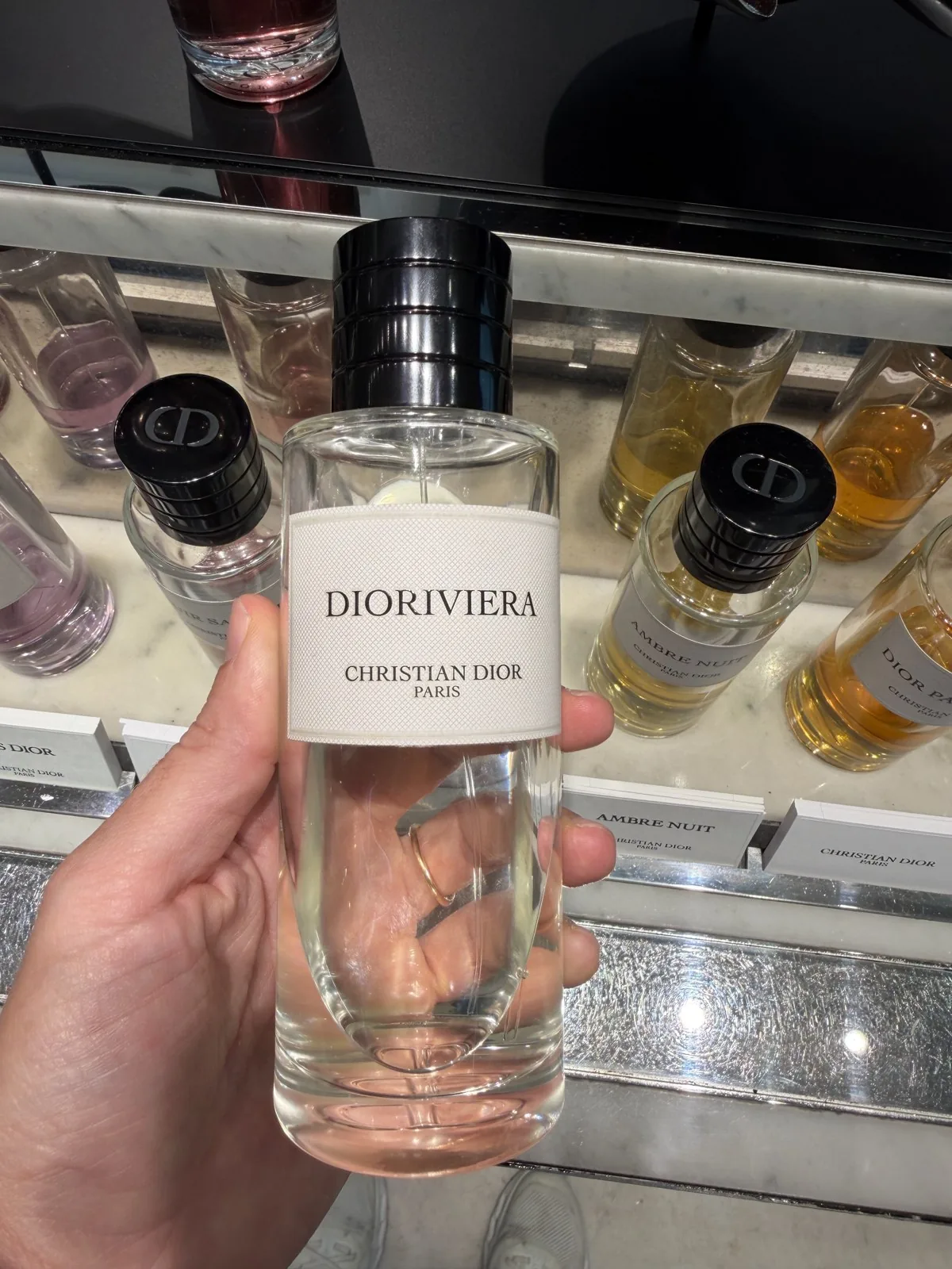 Flakon von Dioriviera von Dior in der Hand, vor den Düften der Collection Privée.