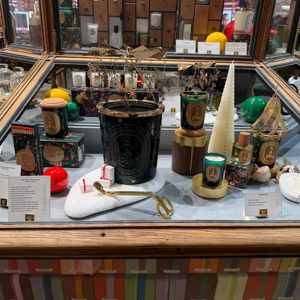 Vitrine de Noël Diptyque avec les bougies Sapin, des boules de Noël et un calendrier de l'Avent.