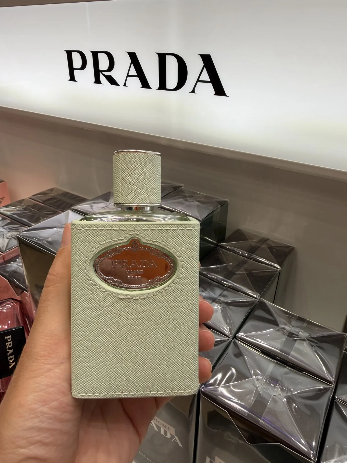 Flakon von Infusion d'Iris von Prada in der Hand, unter dem Schriftzug des Hauses.