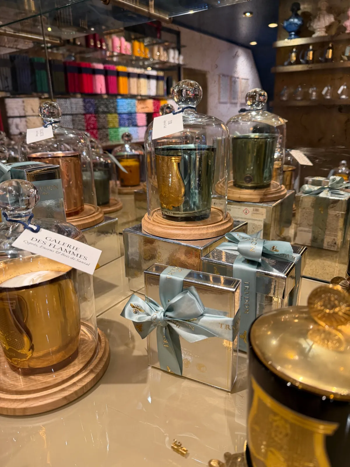 Bougie Fir de Trudon sous cloche en verre, à côté de paquets cadeaux argentés.